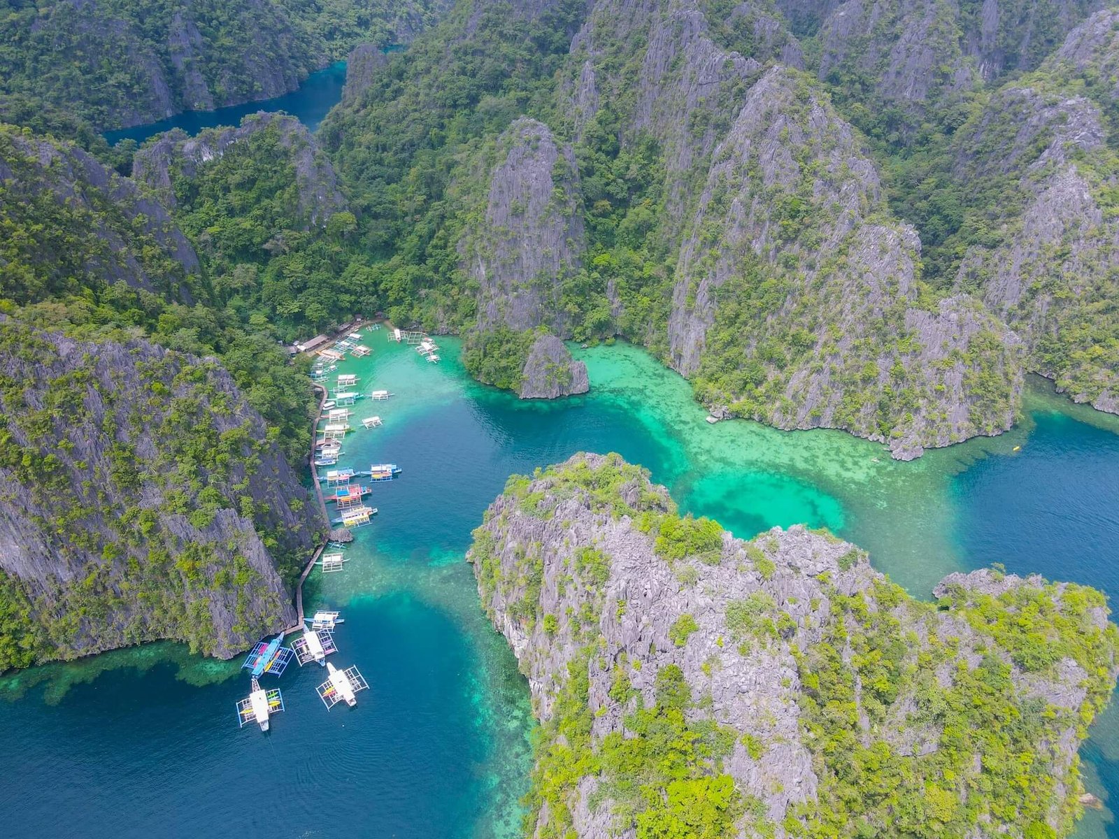 Bangka boats anchored in a turquoise lagoon below limestone cliffs in Coron, Palawan