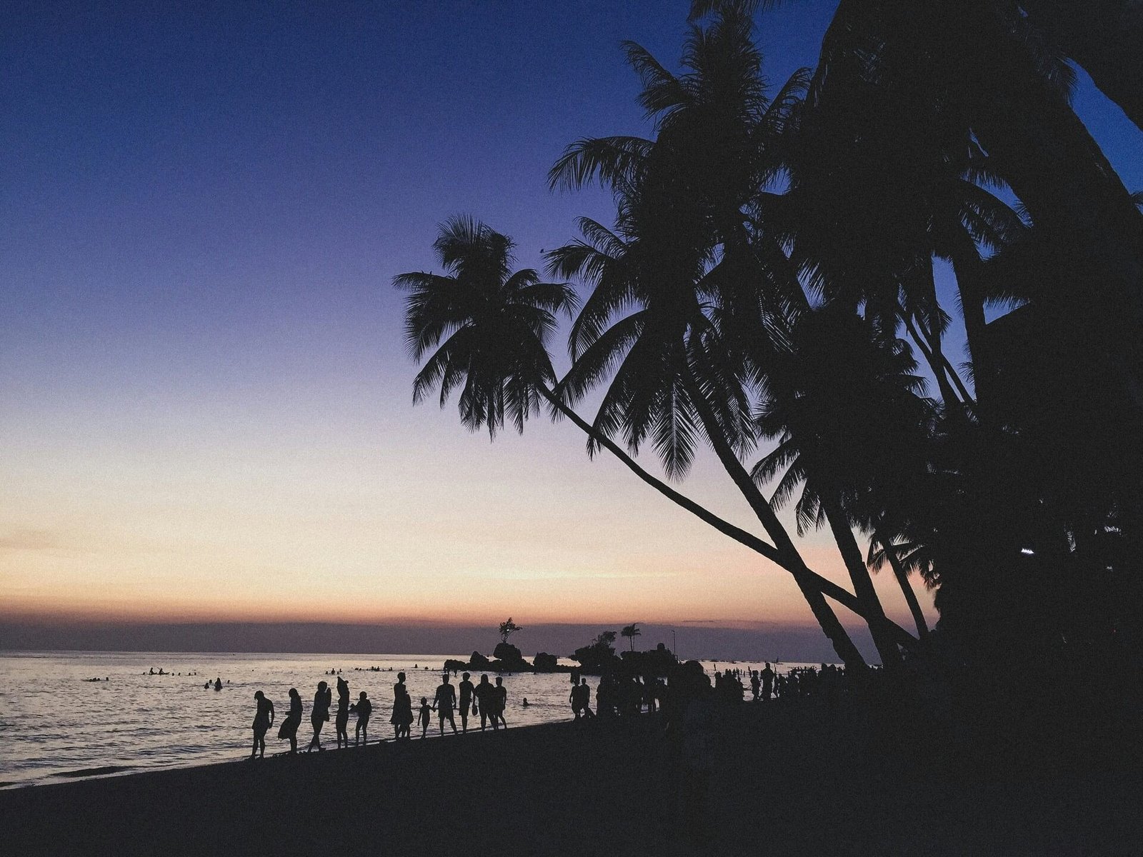 Silhouettes of people and palm trees on a Boracay beach at sunset