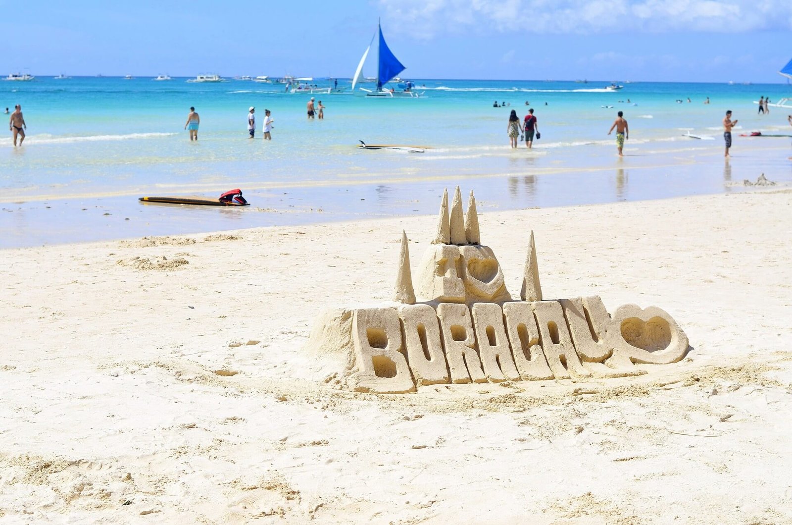Sand sculpture spelling Boracay on a Boracay beach with swimmers in calm water