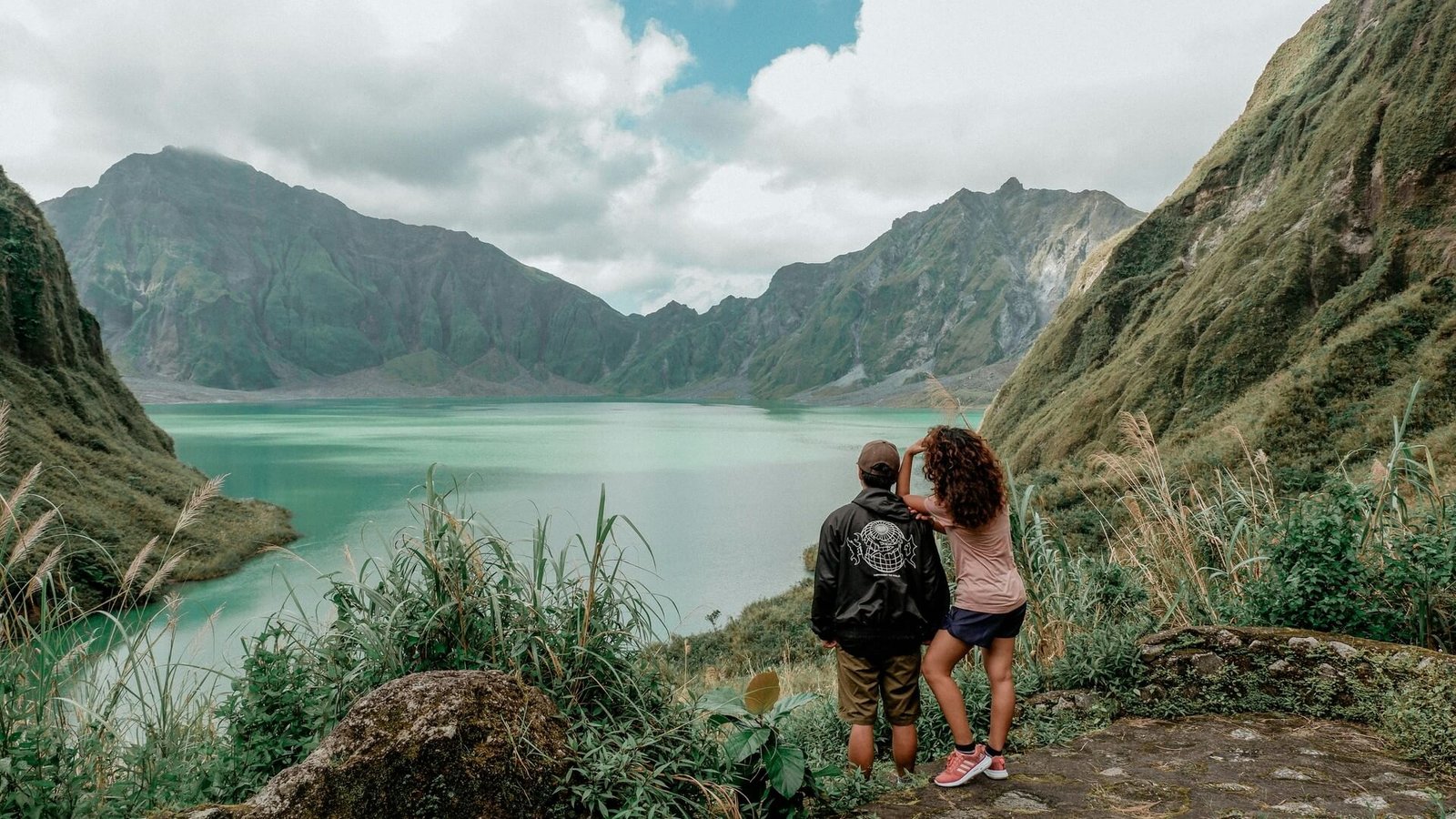 Two hikers looking out over the turquoise Mt Pinatubo crater lake