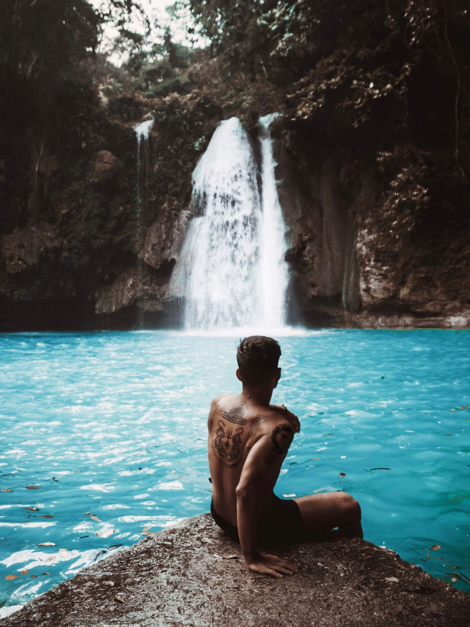 Man sitting on a rock looking at Kawasan Falls in Badian, Cebu