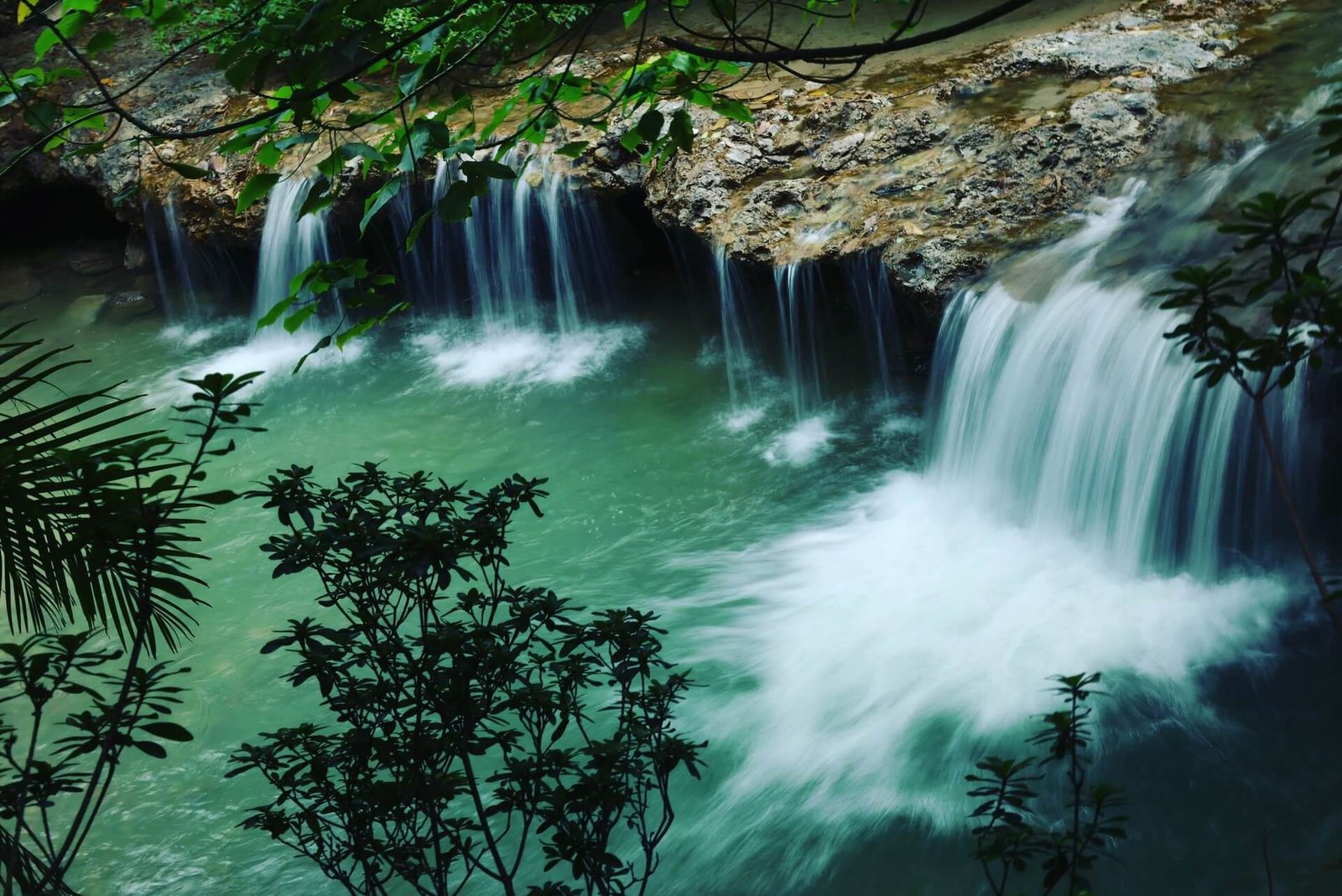 Tiered waterfall spilling into turquoise pools in a tropical forest